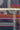 A close-up of a navy blue patterned fabric with geometric white, orange, and pink stripes and curved line motifs, shown with a measuring tape across the middle for scale.