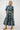 A woman modeling a short-sleeve midi shirt dress with a colorful abstract geometric print on a dark teal background, 