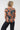 A woman viewed from behind wearing a short-sleeve top with a dark teal background and a large orange abstract circle pattern, 