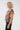 A woman with curly blonde hair is shown from the side, wearing a short-sleeve top with a dark teal background and a large orange floral pattern, 