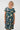A woman modeling a short-sleeve A-line dress with a dark teal green background and a colorful abstract pattern of circles, waves, and geometric shapes in cream, yellow, pink, and blue.