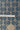 A close-up of a woven fabric with a repeating geometric pattern in dark blue on a warm beige background, with a white measuring tape laid horizontally across the middle for scale.
