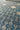 A close-up of patterned fabric with a repeating geometric design in blue and beige, showing the woven texture and rolled edge at the top.