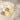 A pair of silver-tone hoop earrings with small, translucent yellow flower charms, resting on a textured beige linen fabric under soft, natural sunlight.