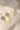 A pair of silver-tone hoop earrings with small, translucent yellow flower charms, resting on a textured beige linen fabric under soft, natural sunlight.