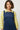 Woman wearing a blue pinafore dress over a yellow floral shirt against a white background