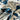 A close-up of a draped fabric with a bold, dark teal blue abstract floral and leaf pattern on an off-white background.
